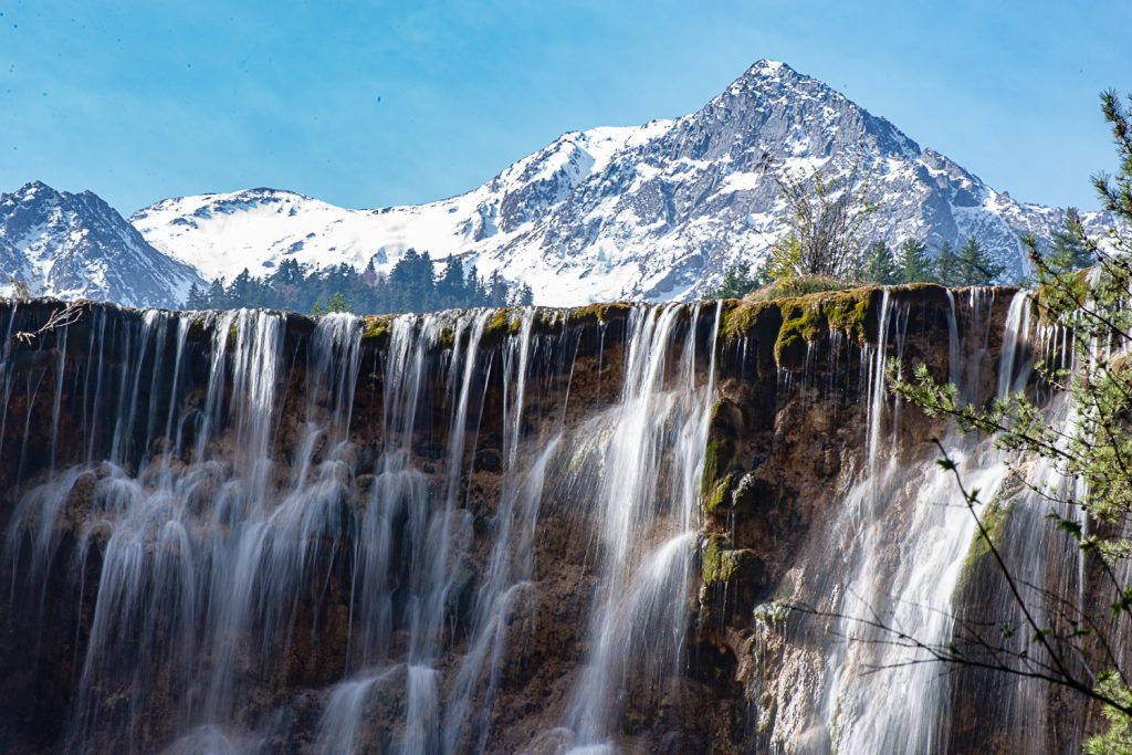 Silky waterfalls in front of a snow covered mountain within Juizhaigou Nature Reserve in Sichuan Province, China